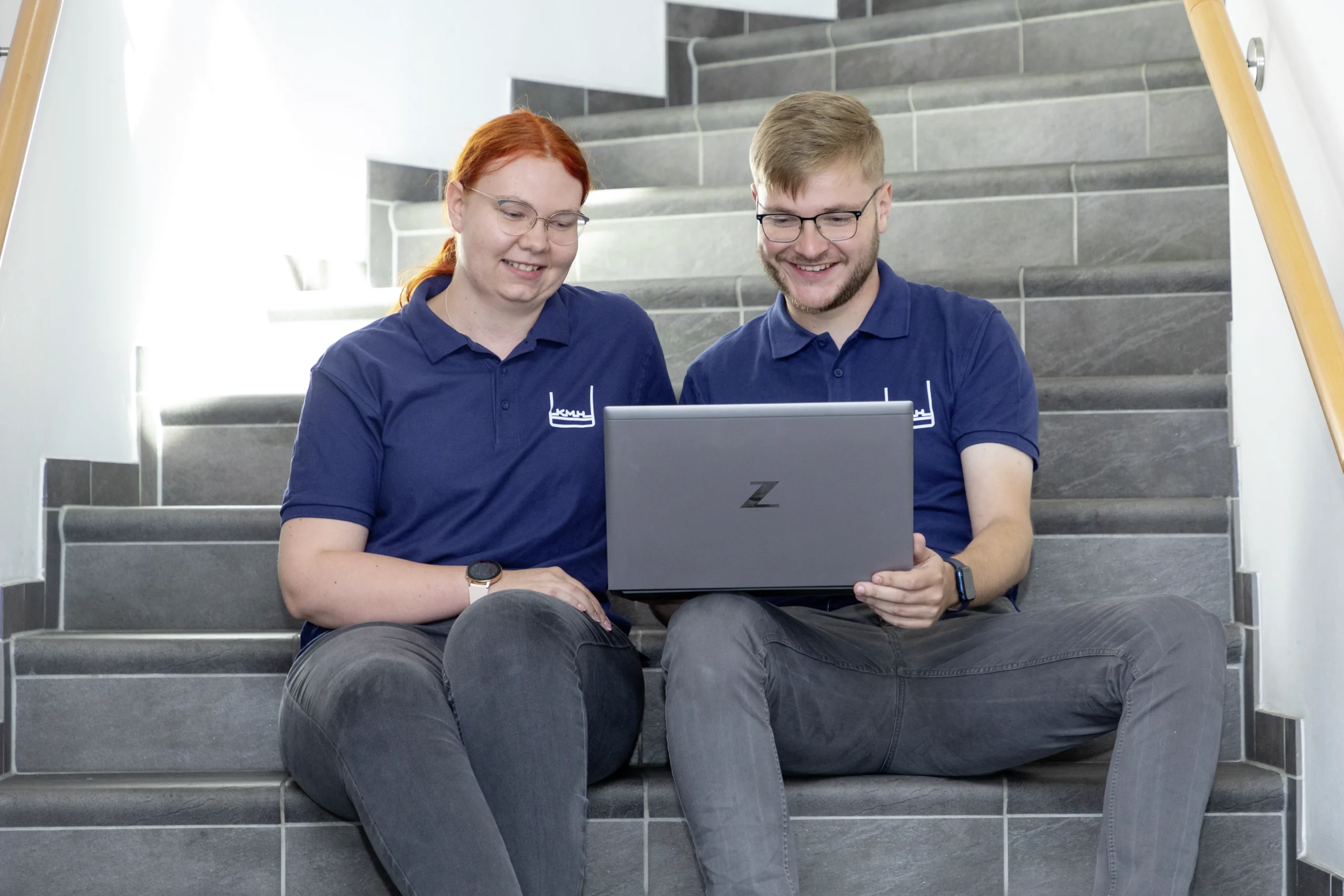 Zwei Auszubildende sitzen auf der Treppe mit Laptop auf dem Schoß